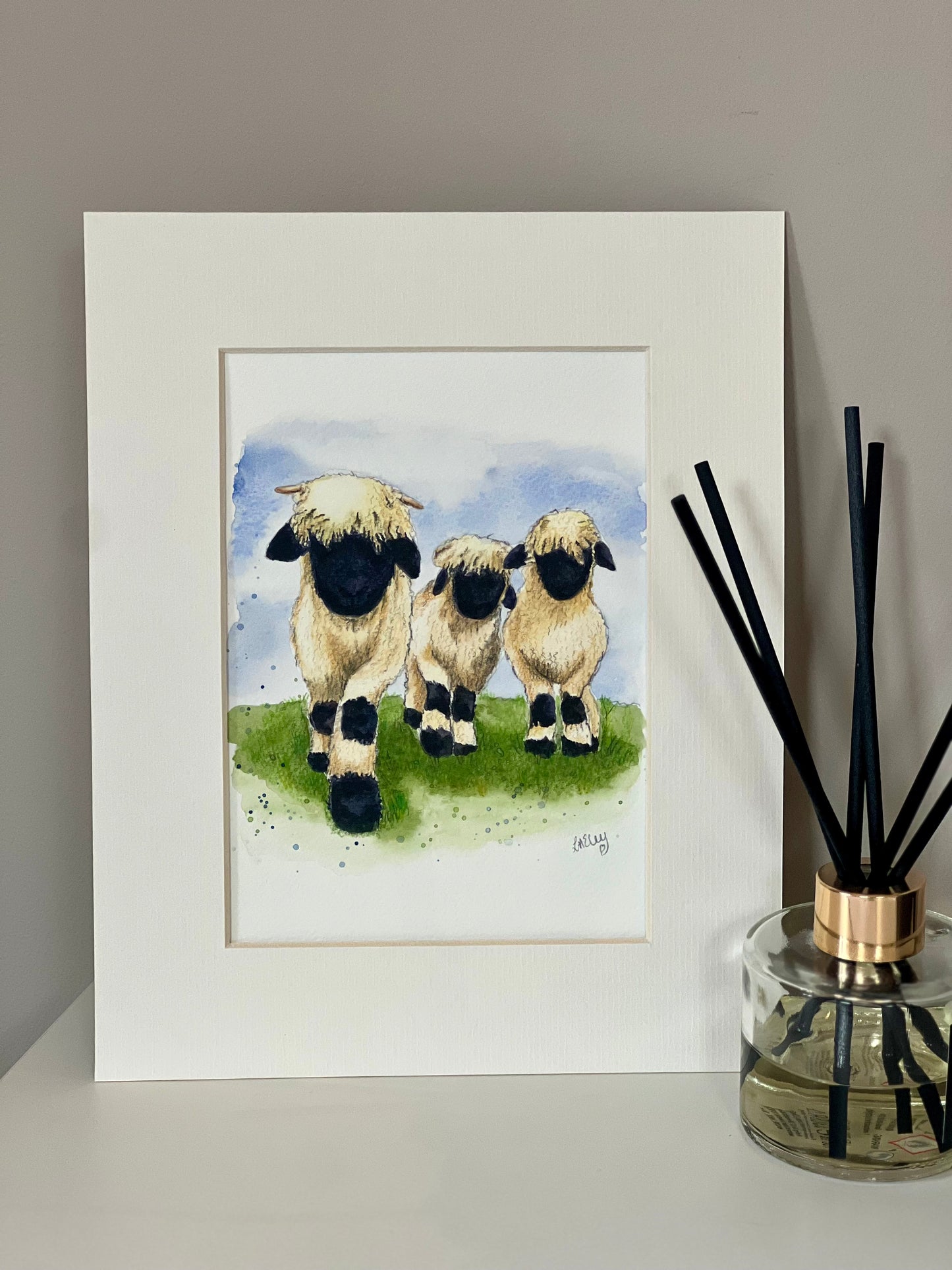 A watercolor painting of three Valais Blacknose sheep standing in a field, with an ivory-toned mount.