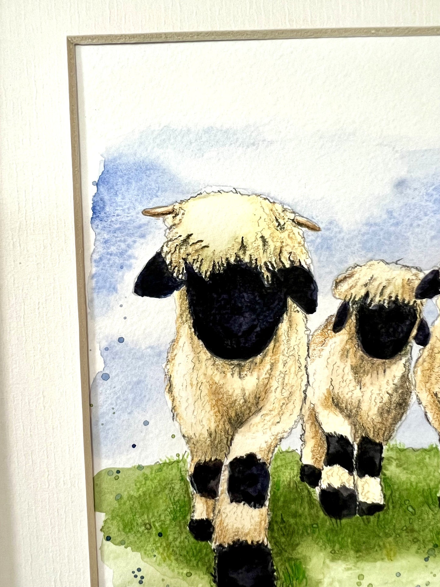 Close up of a watercolor painting of three Valais Blacknose sheep standing in a field, with an ivory-toned mount.