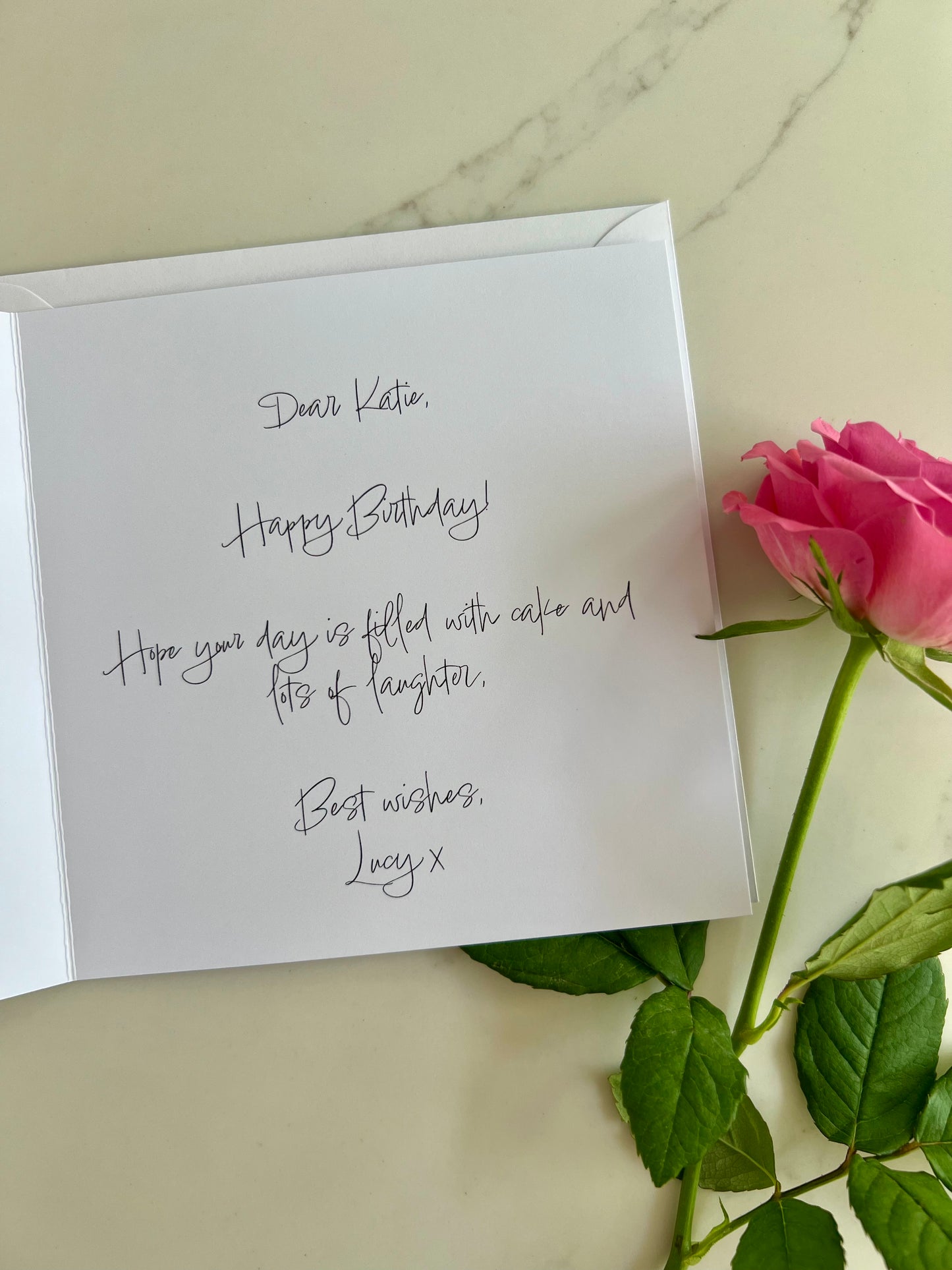 Personalised message inside a birthday card with a pink rose on a marble surface