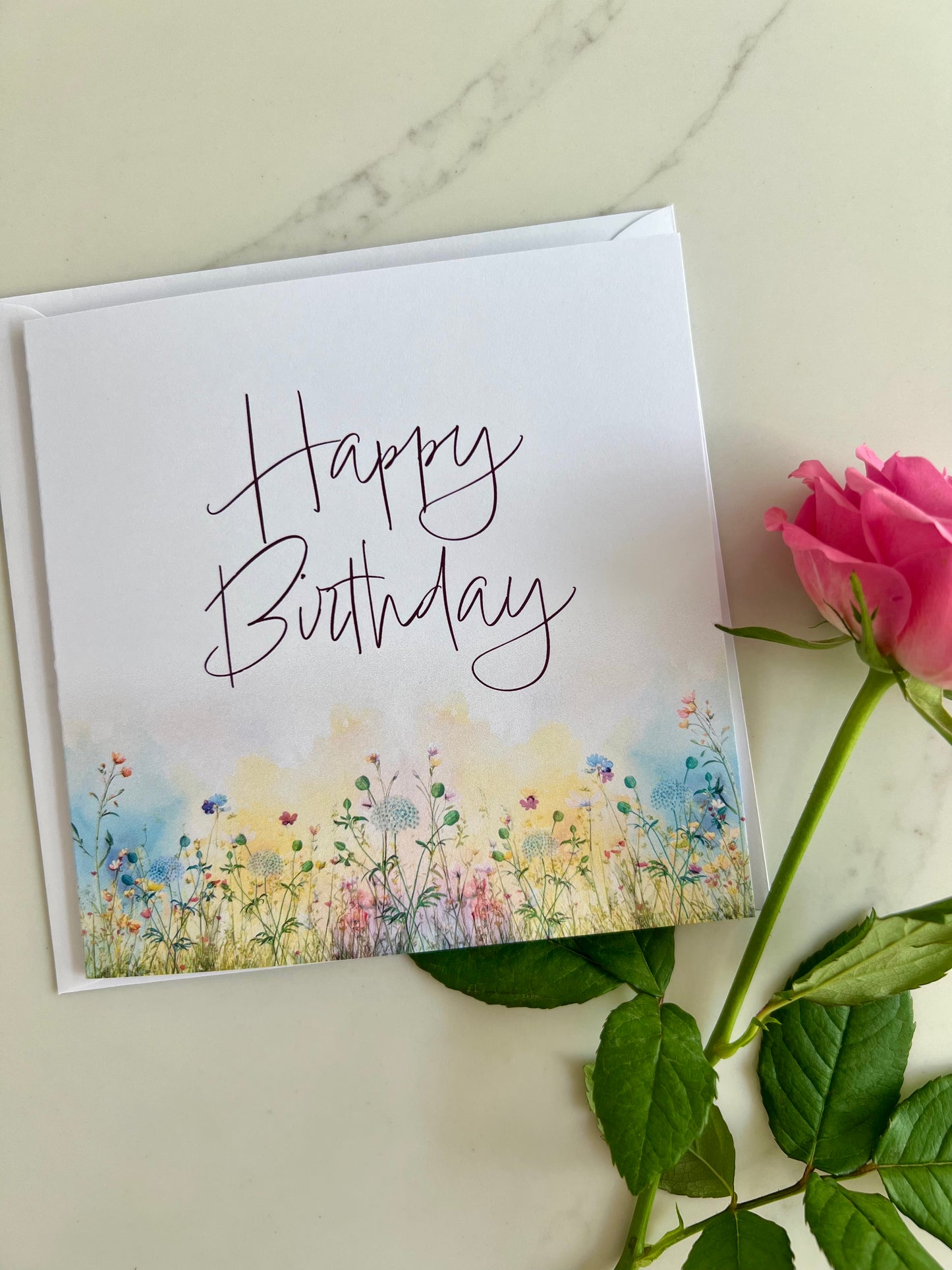 Personalised Birthday card with floral design and 'Happy Birthday' text, accompanied by a pink rose on a marble surface.