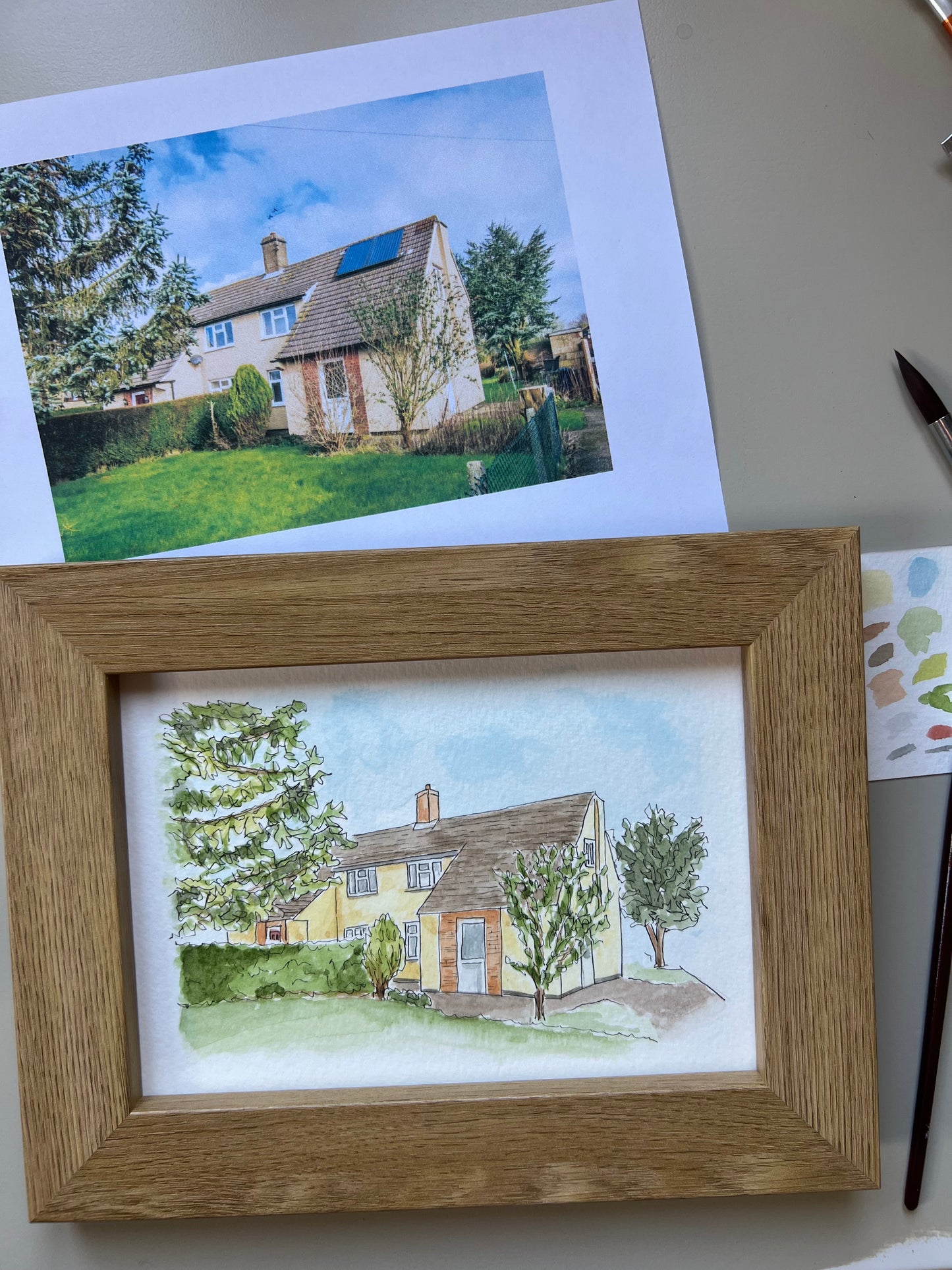 Framed watercolour painting of a house with trees with original photo in background.