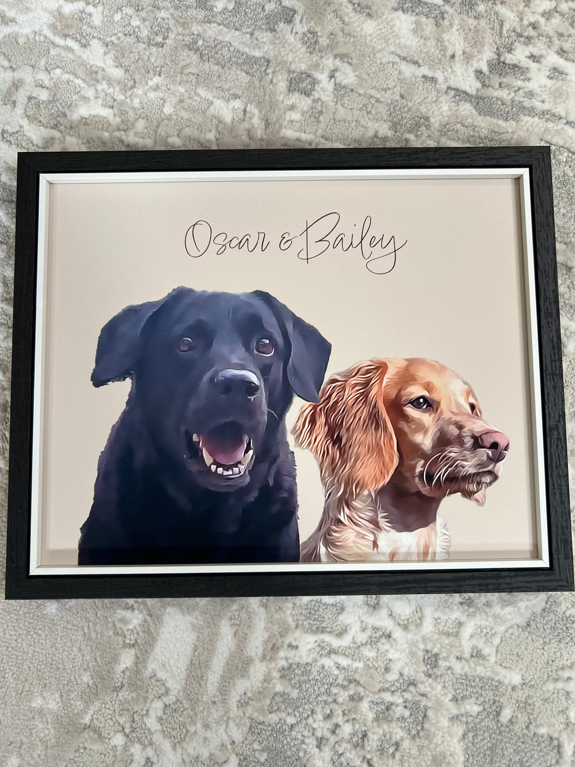 Framed portrait artwork of two dogs, one brown spaniel and one black retriever in a black frame, on a textured floor.