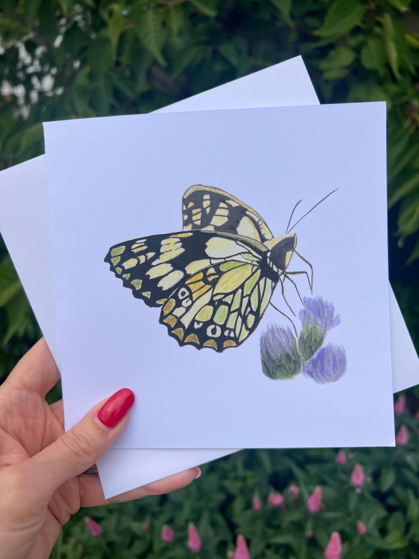 Butterfly illustration on a card with metallic accents held by a hand against a natural background.