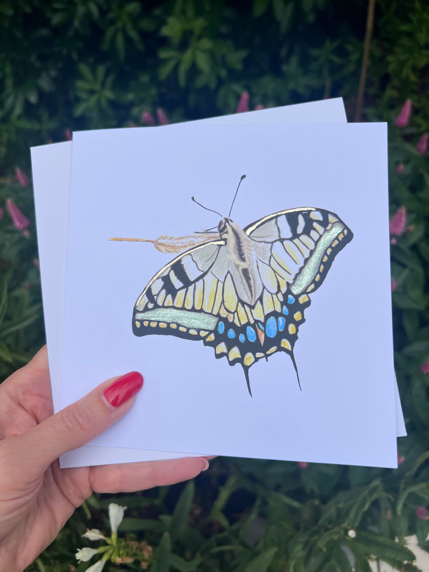 Hand holding a card with a Swallowtail Butterfly illustration with green and gold metallic finish with nature background.