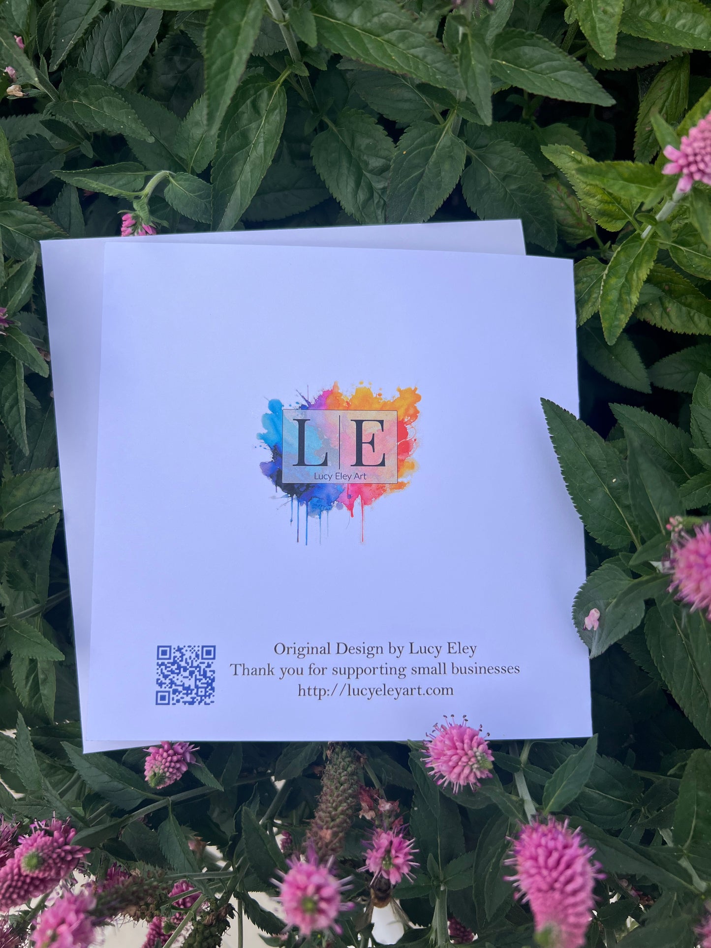 Reverse of Card with colorful design and text on a green leafy background with pink flowers