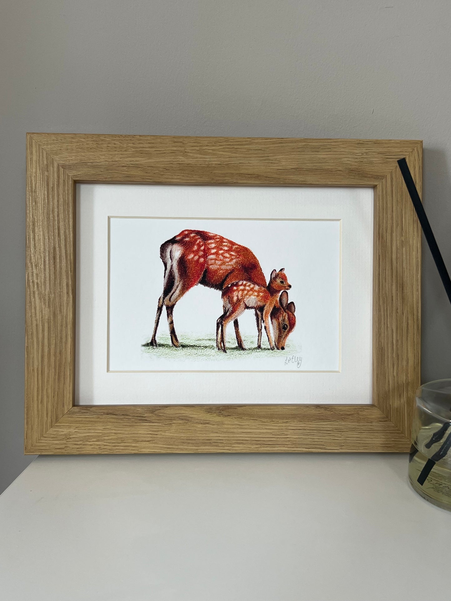 Framed artwork of a Sika Deer Mother and Fawn in vibrant oranges and reds on a white background in a wooden oak style frame.