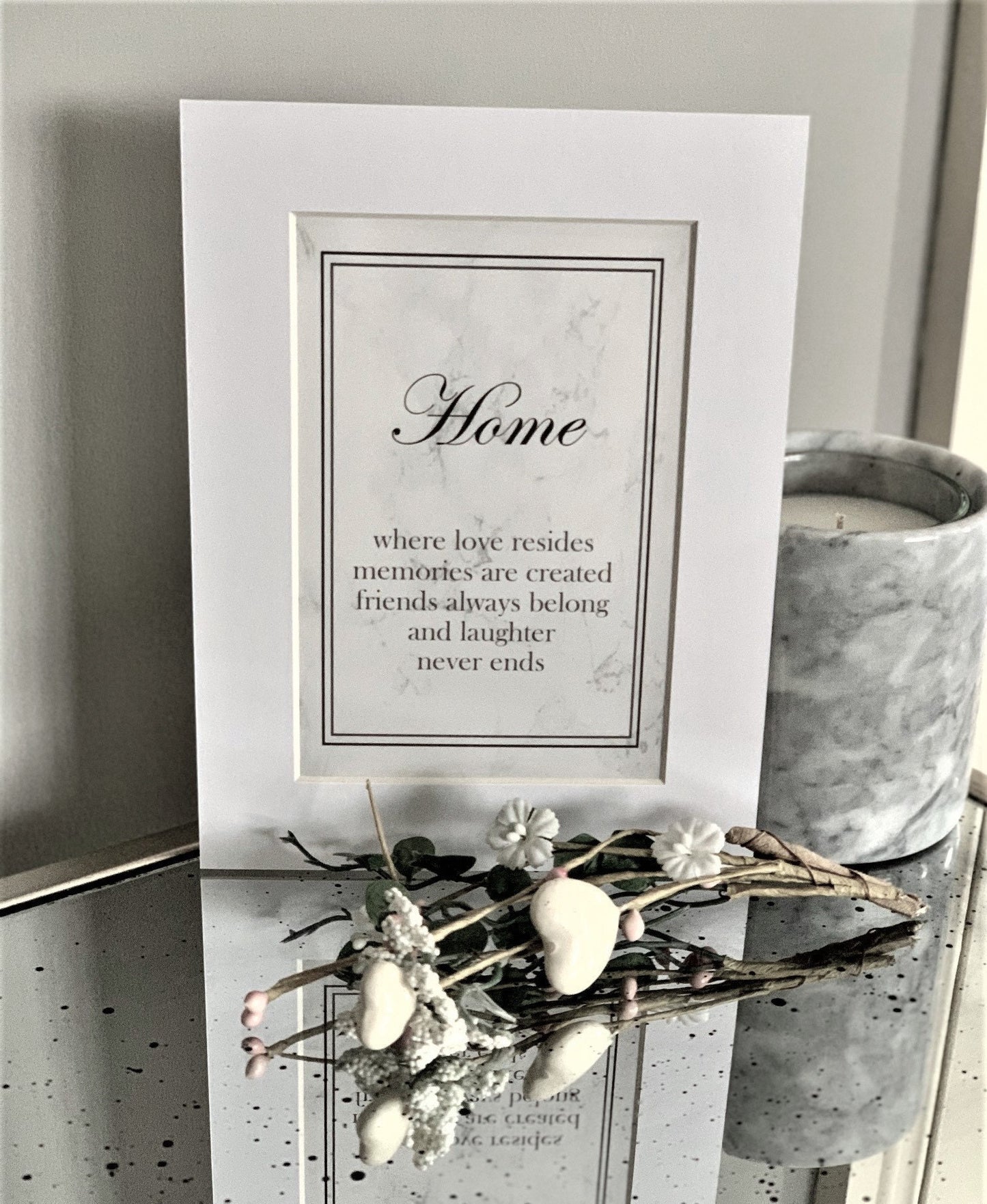A framed print with the text 'Home - where love resides, memories are created, friends always belong, and laughter never ends' on a grey marble background and white mount.