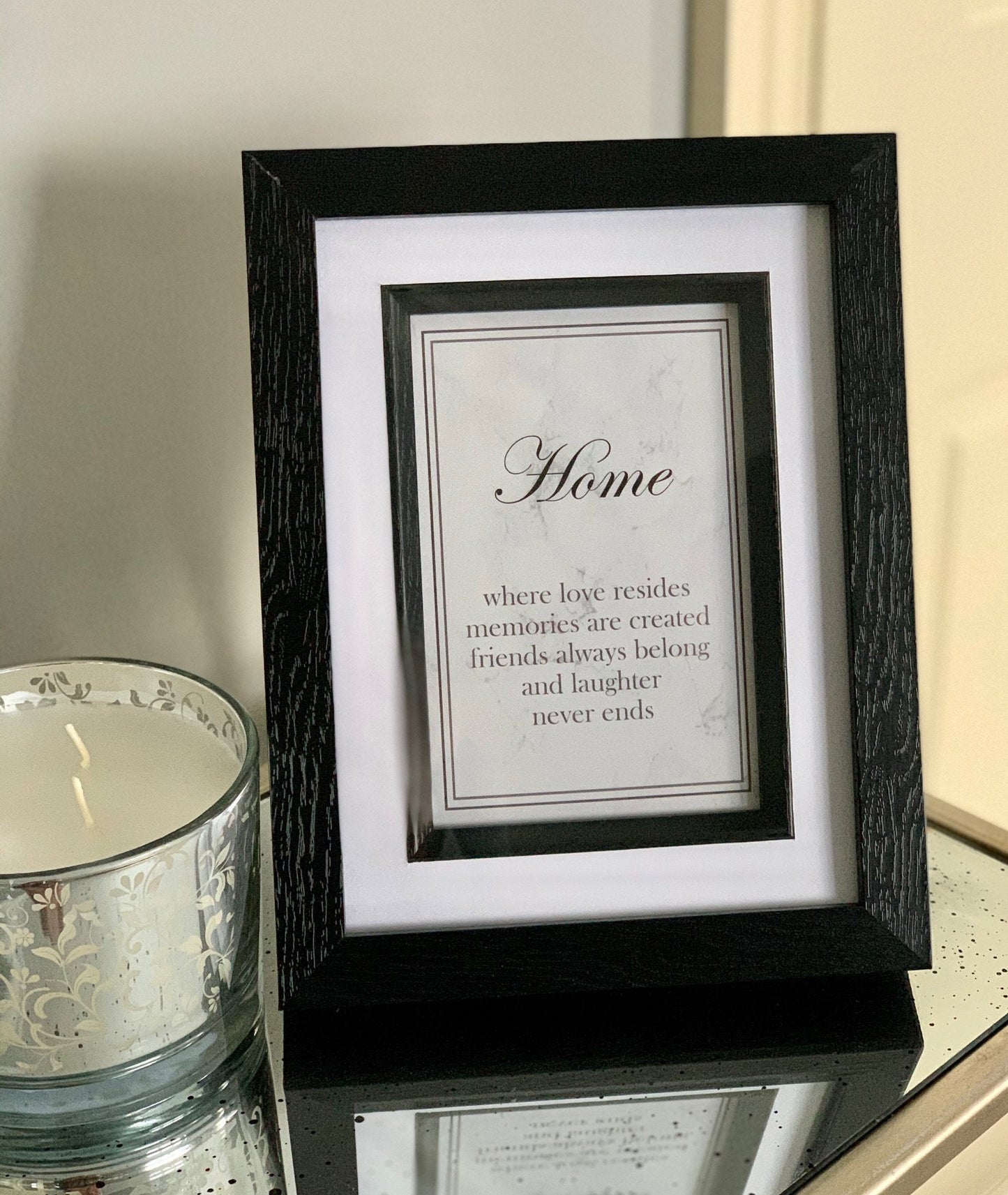 A framed print with the text 'Home - where love resides, memories are created, friends always belong, and laughter never ends' on a grey marble background and black frame.