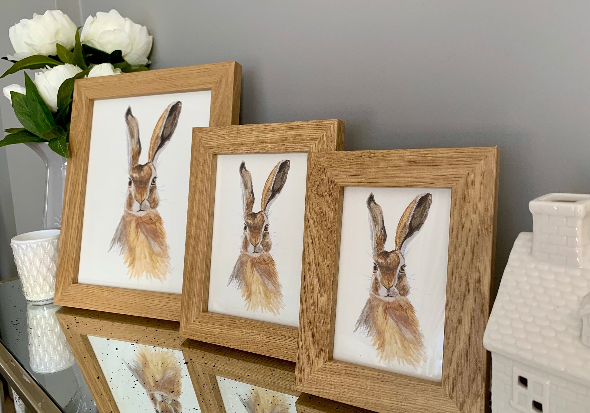 Set of 3 Watercolour hare paintings in brown and grey tones in a oak finish wooden frames showing different sizes.