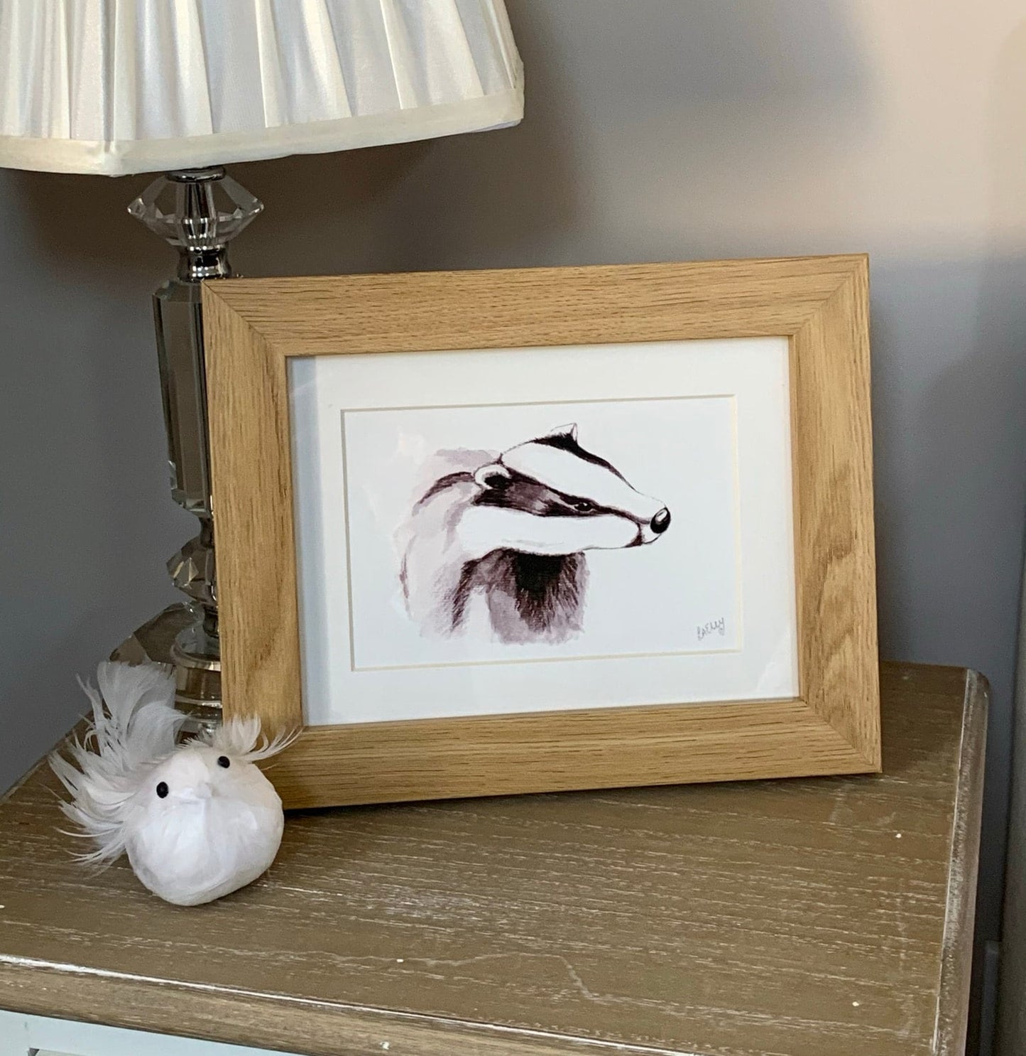 Watercolour young badger painting in grey tones in a oak finish wooden frame with white mount.