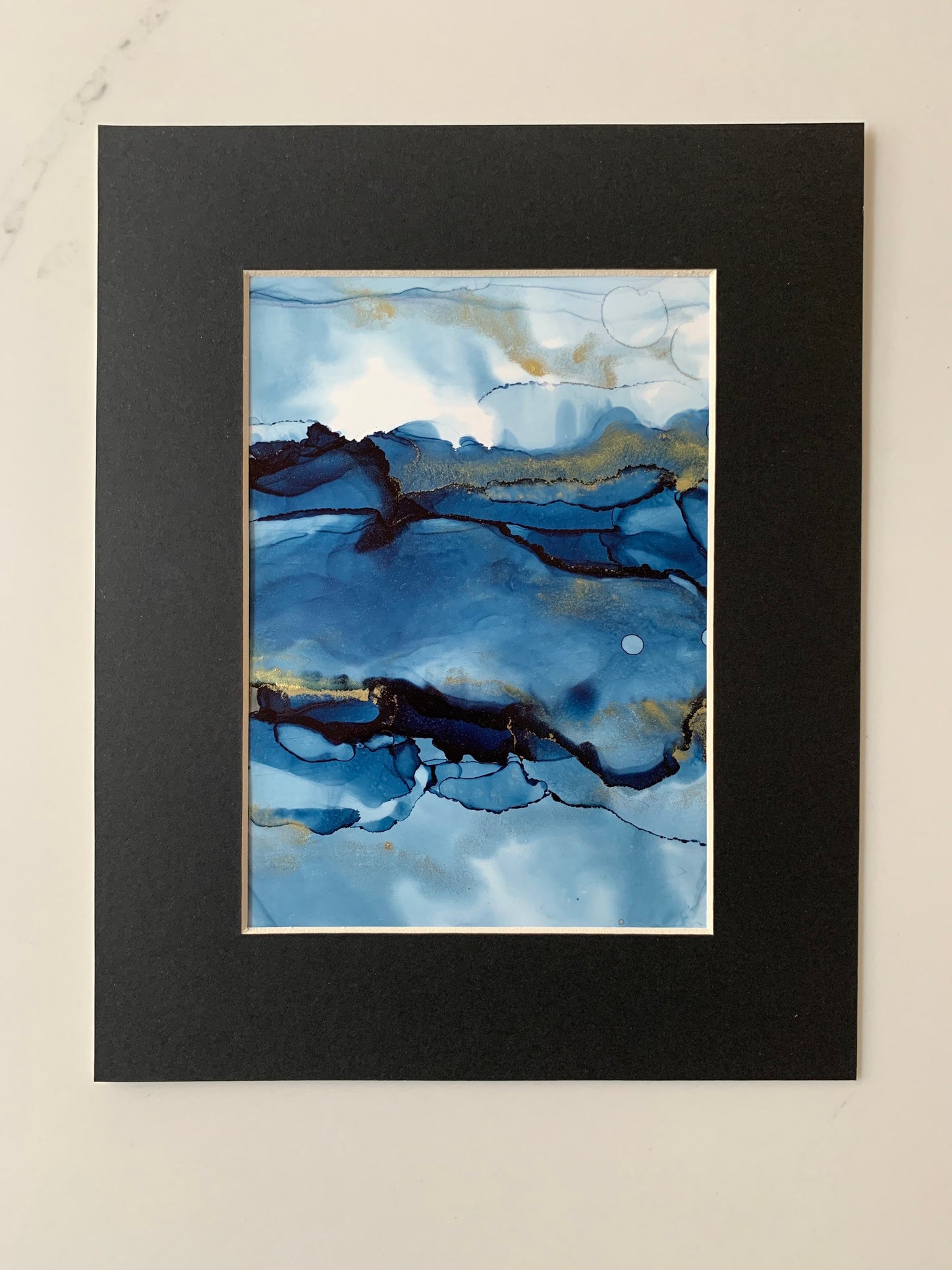 An A5 size contemporary ink painting featuring blue and metallic colours with gold shimmers, presented in a black mount.