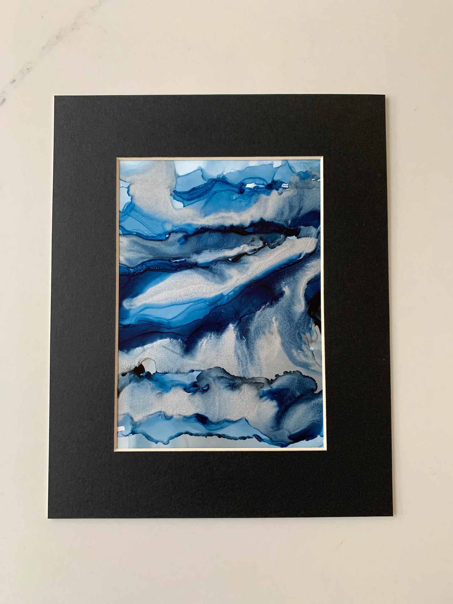 An abstract ink painting in shades of blue and silver, presented in a black mount.
