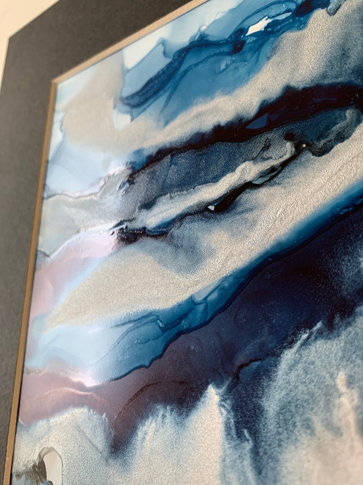 An abstract ink painting in shades of blue and silver, presented in a black mount.