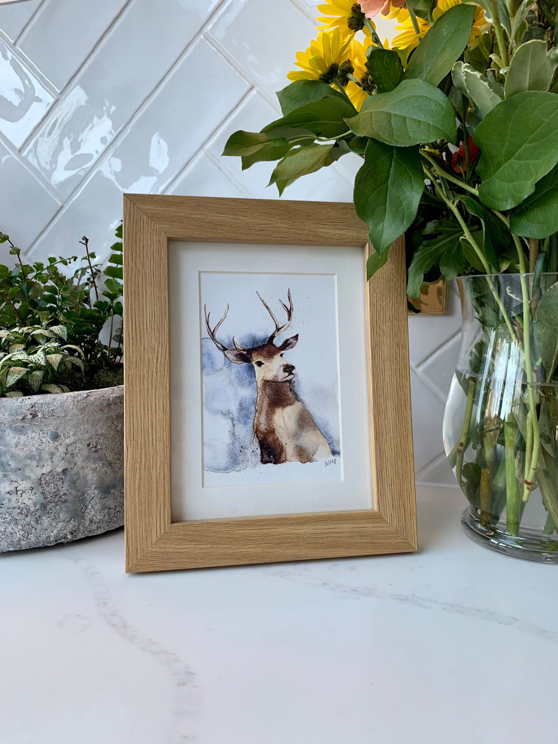 Watercolour stag in brown, grey and blue tones in a white mount and wooden frame.