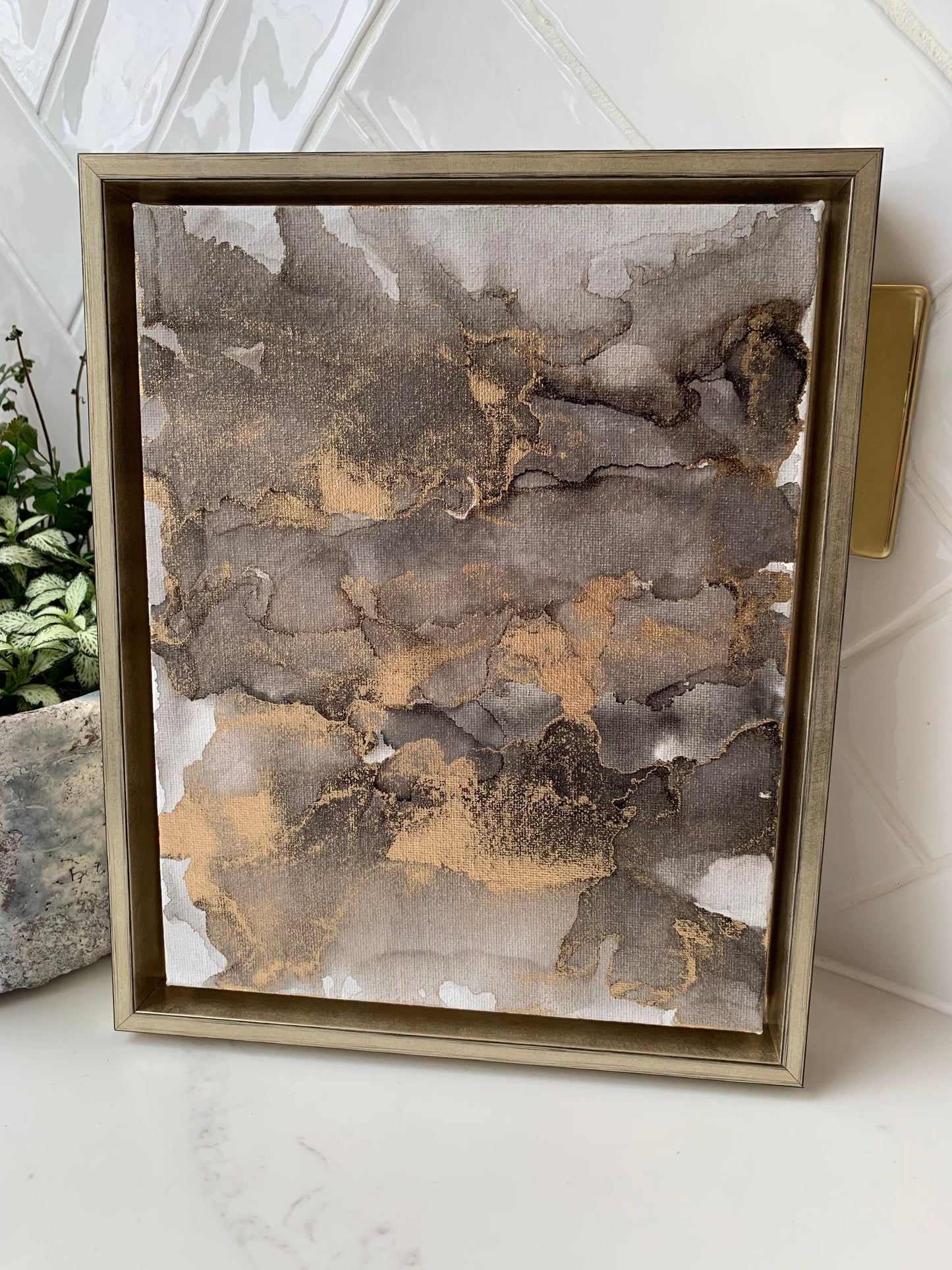 An abstract grey black and gold alcohol ink painting on canvas with a gold frame, displayed against a white background.