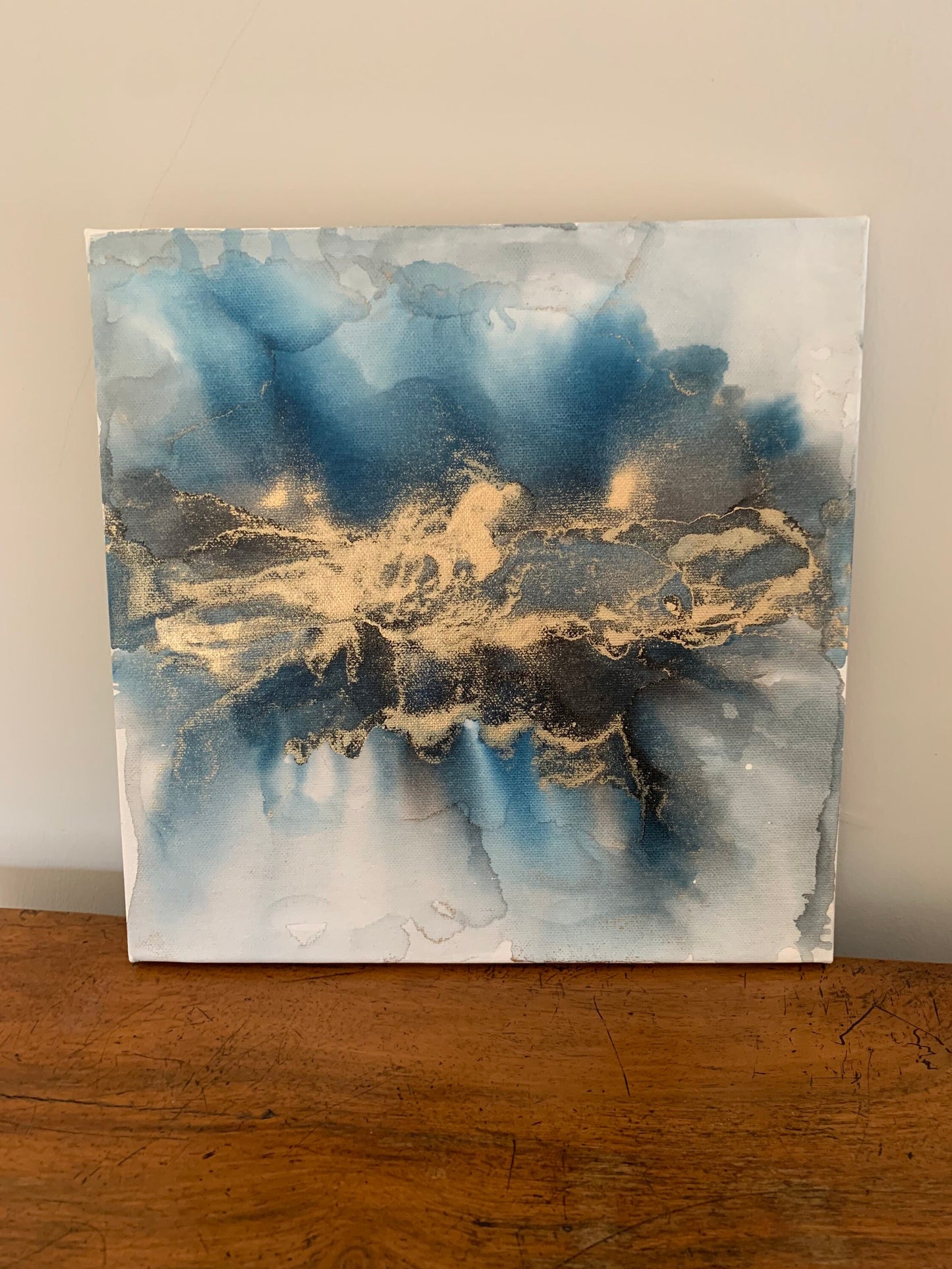 A one-off statement canvas painting featuring an abstract design in alcohol inks with gold and blue colours, with a metallic finish.
