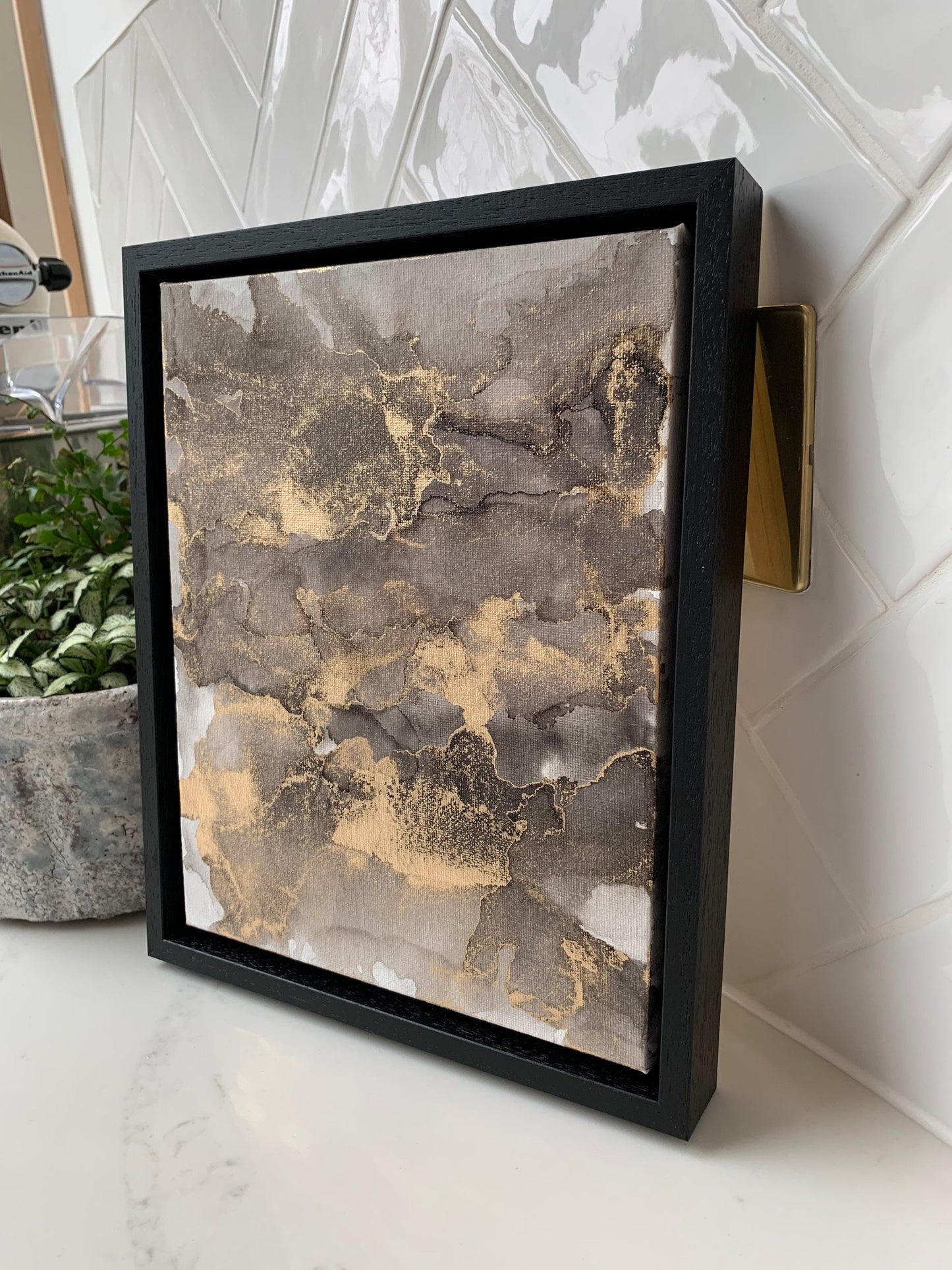 An abstract grey black and gold alcohol ink painting on canvas with a black frame, displayed against a white background.