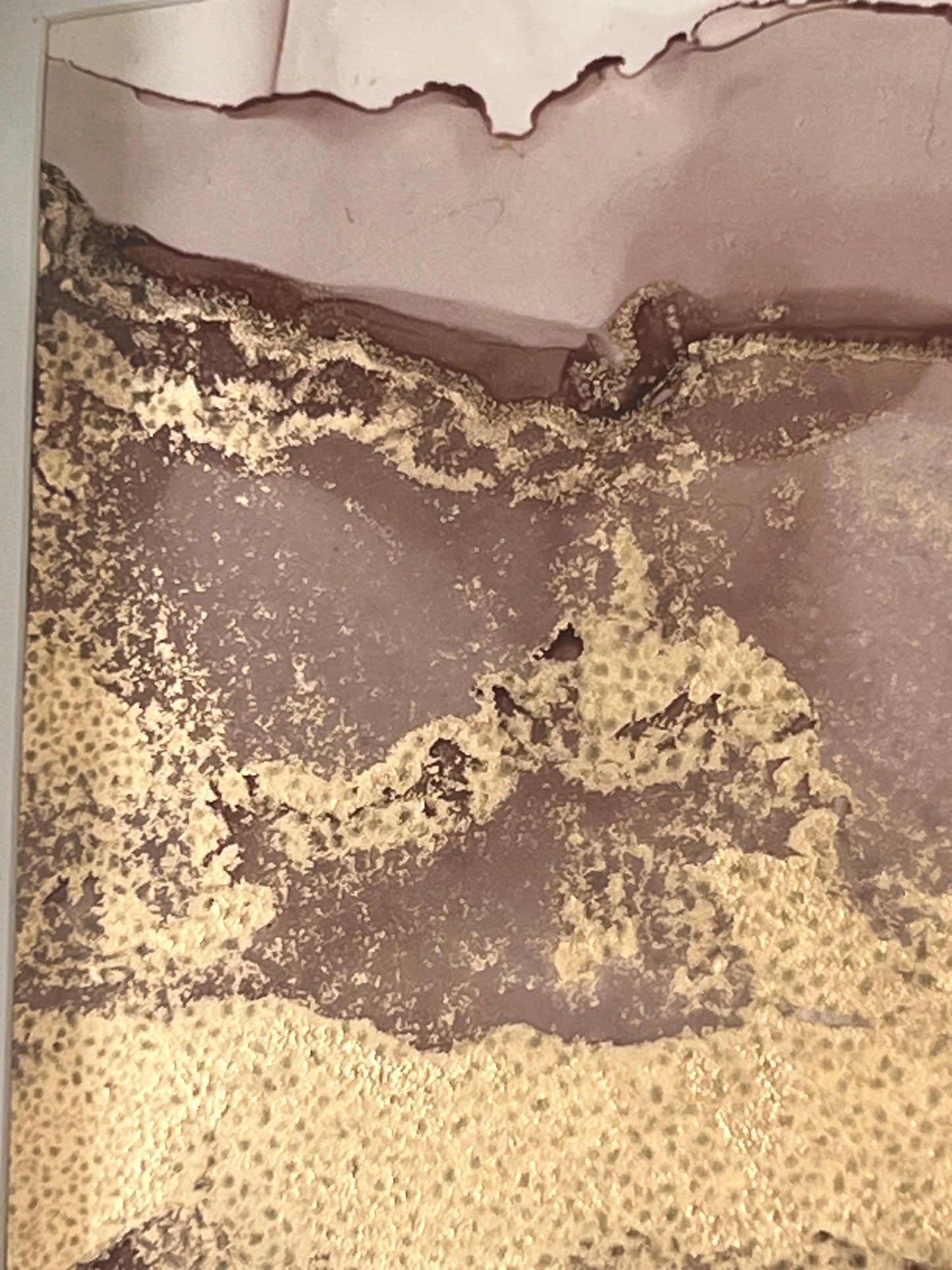Close up of a 7x5 inch alcohol ink abstract painting with soft gold and pink colours, featuring subtle gold shimmers, mounted and framed in a gold foil finished frame.