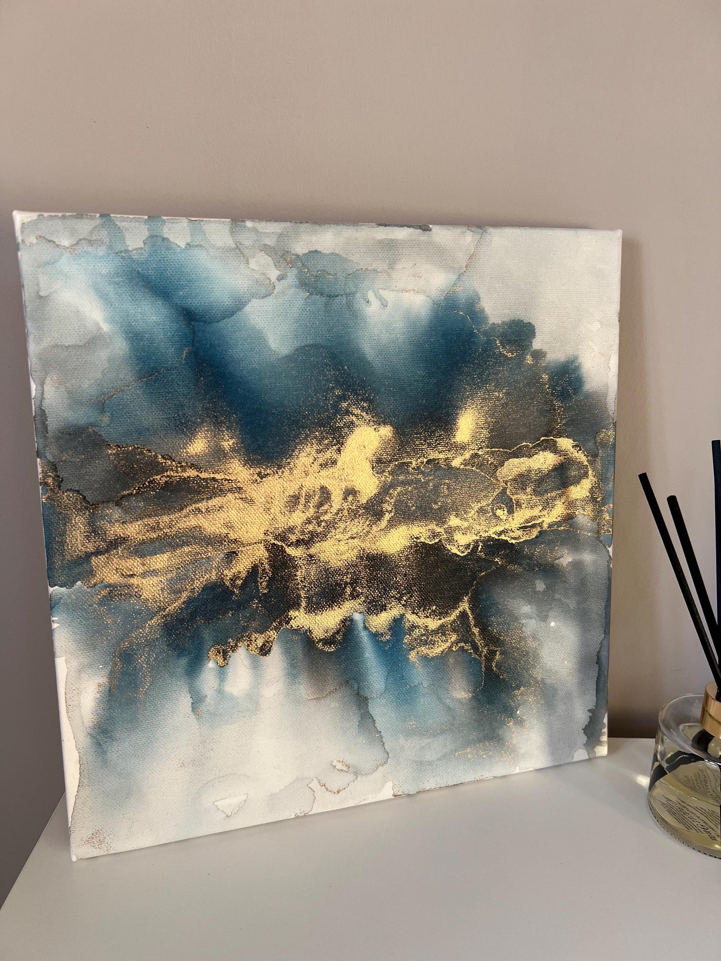 A one-off statement canvas painting featuring an abstract design in alcohol inks with gold and blue colours, with a metallic finish.