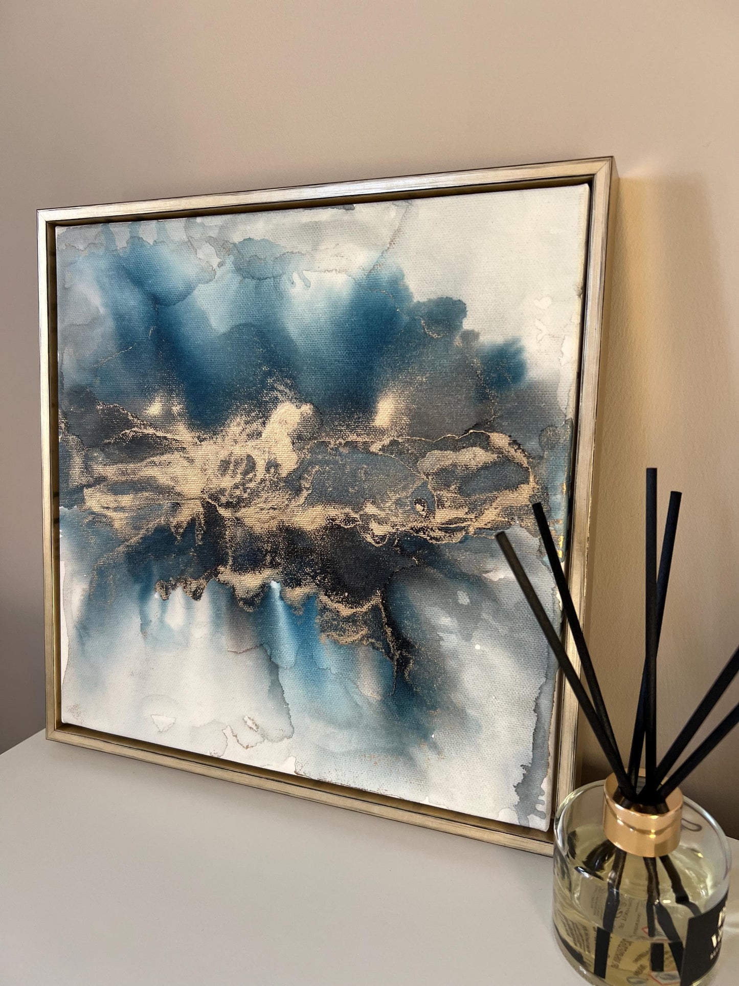 Side view of a one-off statement canvas painting featuring an abstract design in alcohol inks with gold and blue colours, with a metallic finish and in a gold finish box frame.