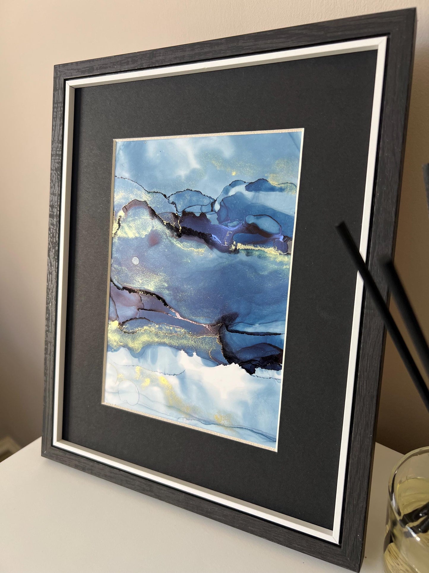 An A5 size contemporary ink painting featuring blue and metallic colors with gold shimmers, presented in a black frame.