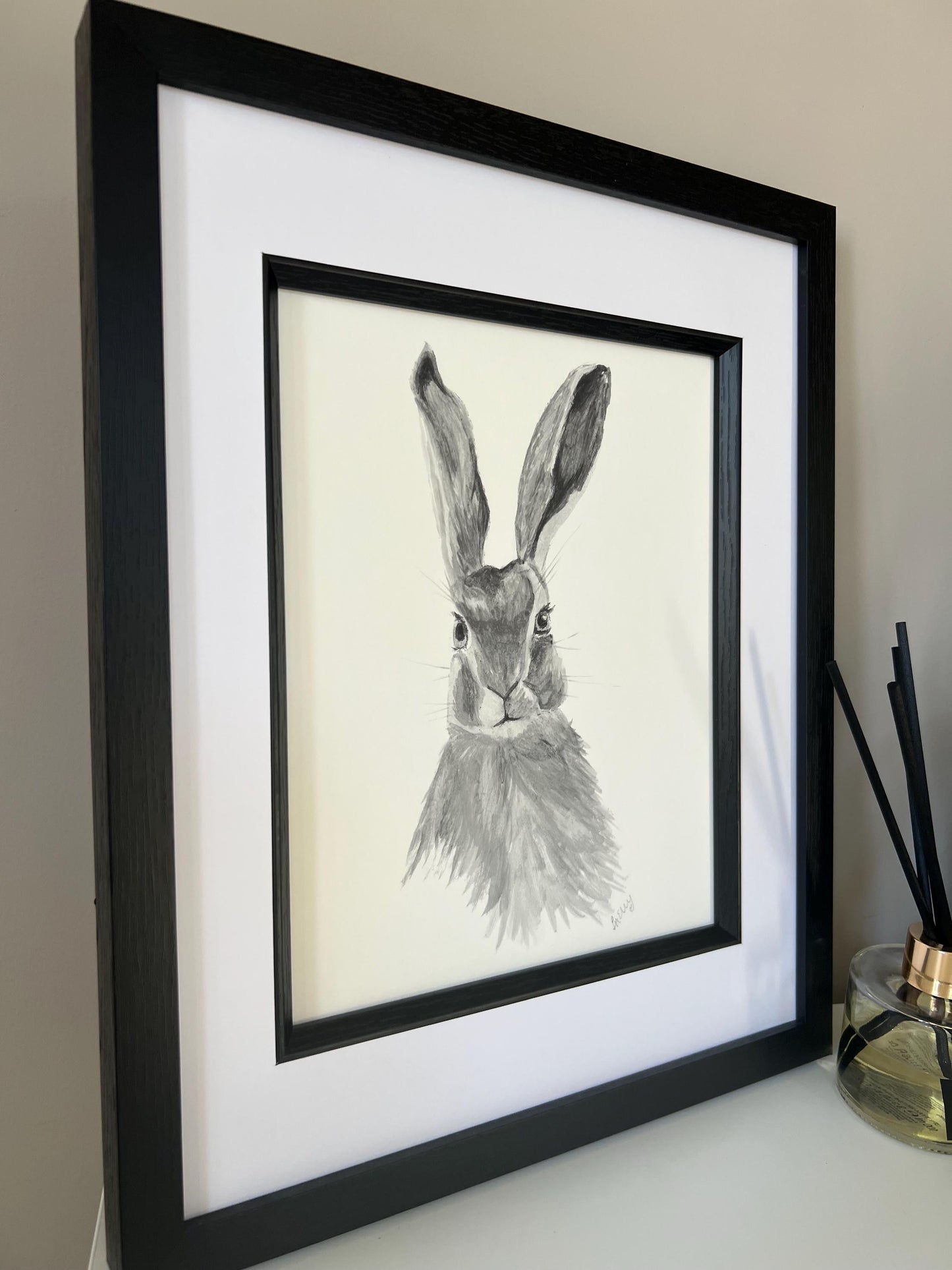 Side view of Watercolour hare in grey tones in a black wooden frame with double mount.
