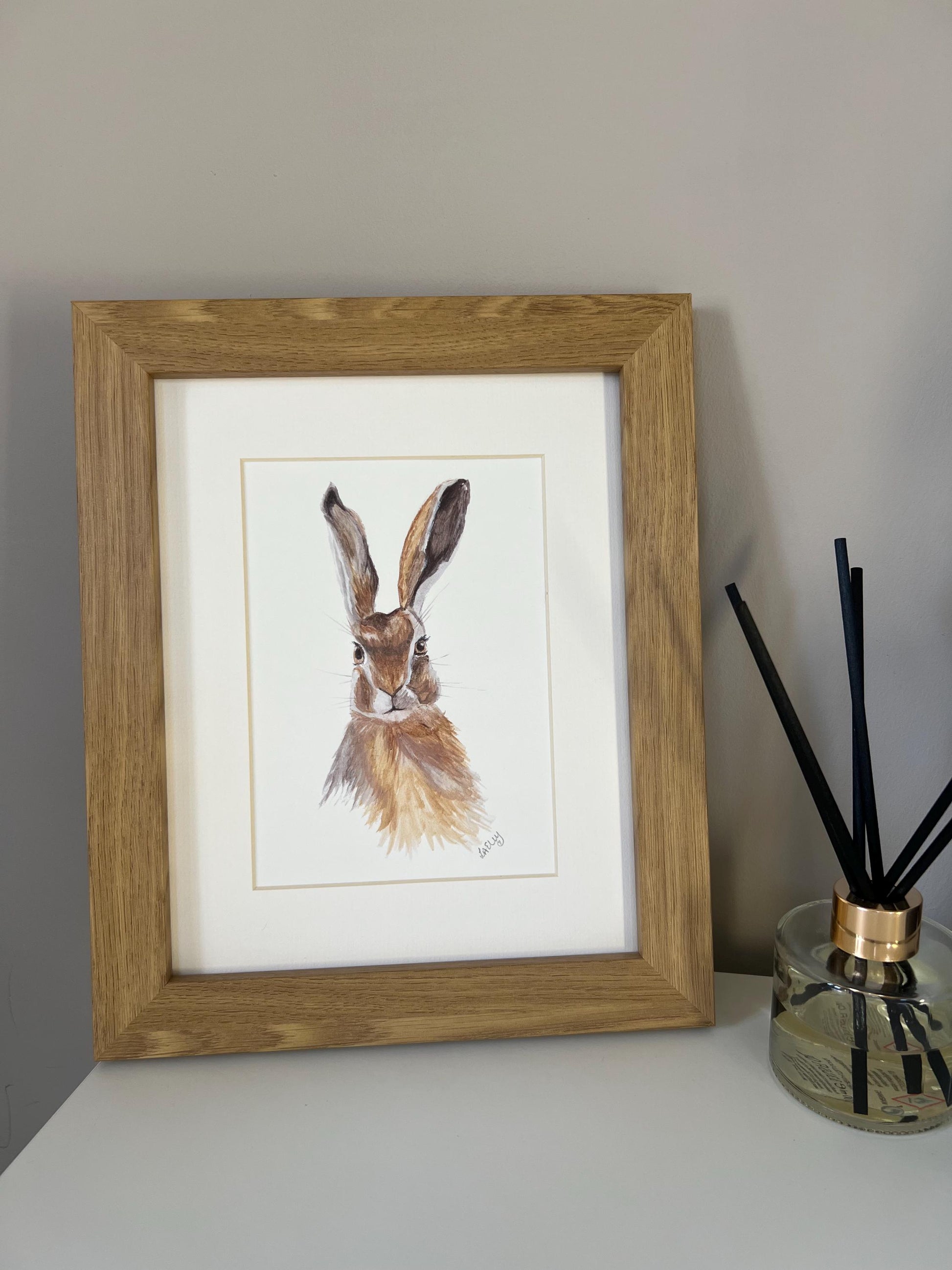 Watercolour hare in brown and grey tones in a oak finish wooden frame with white mount.