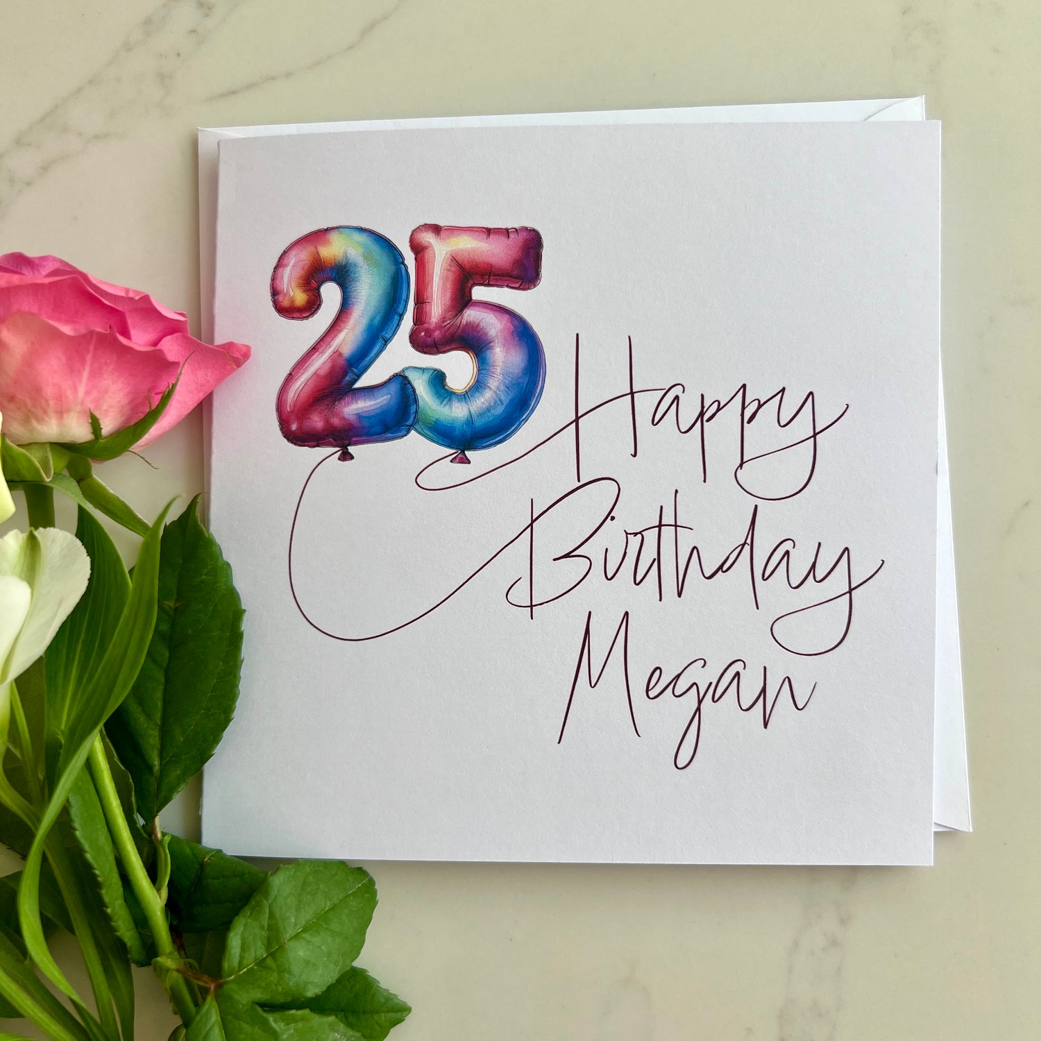 Personalised Birthday card with colourful number '25' in balloons and 'Happy Birthday Megan' text, surrounded by flowers on a light background.