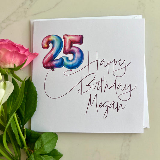 Personalised Birthday card with colourful number '25' in balloons and 'Happy Birthday Megan' text, surrounded by flowers on a light background.