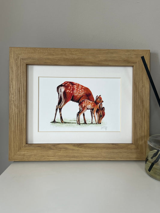 Framed artwork of a Sika Deer Mother and Fawn in vibrant oranges and reds on a white background in a wooden oak style frame. 