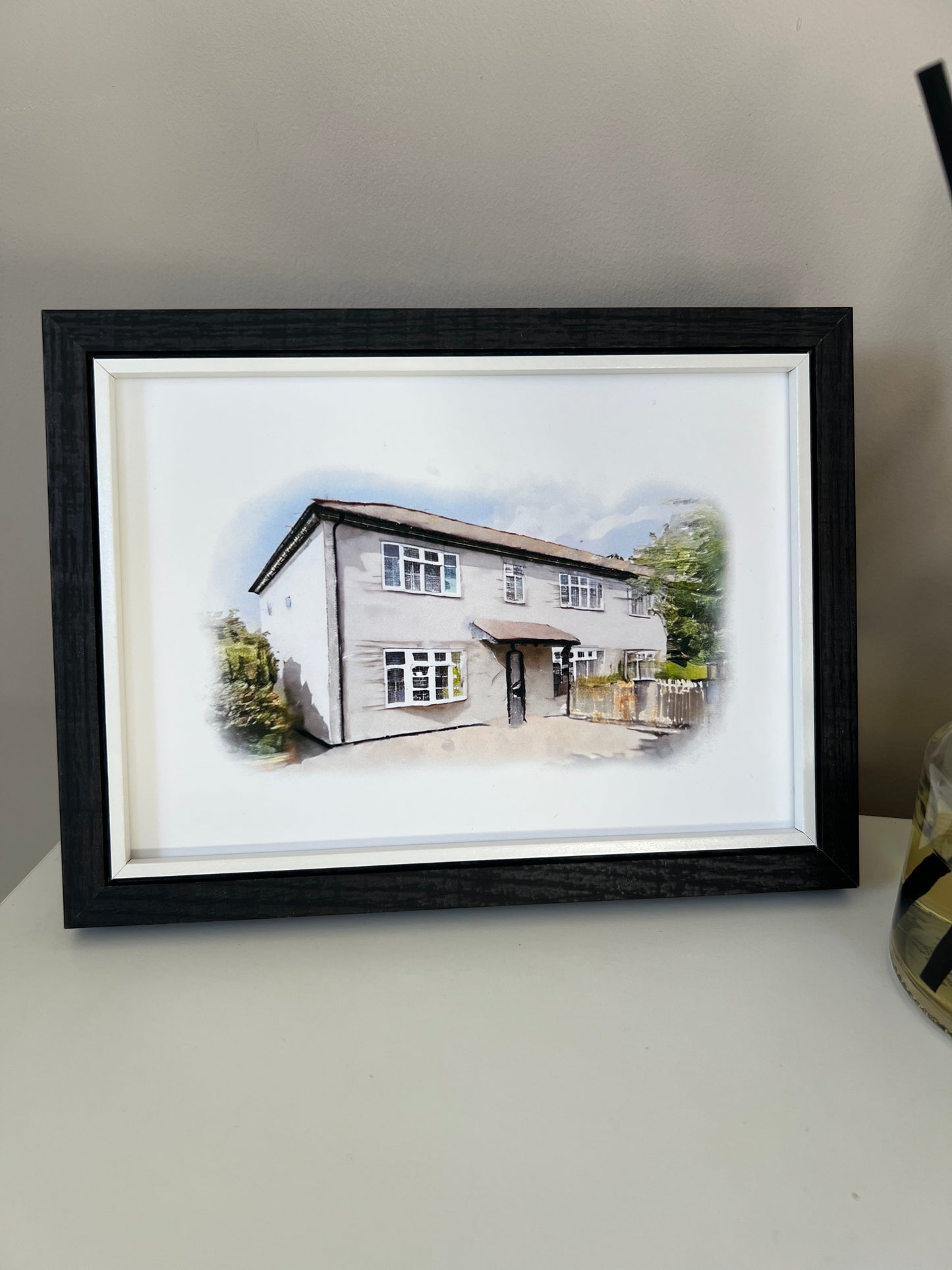 Framed artwork of a cottage house portrait in digital watercolour in a black frame.