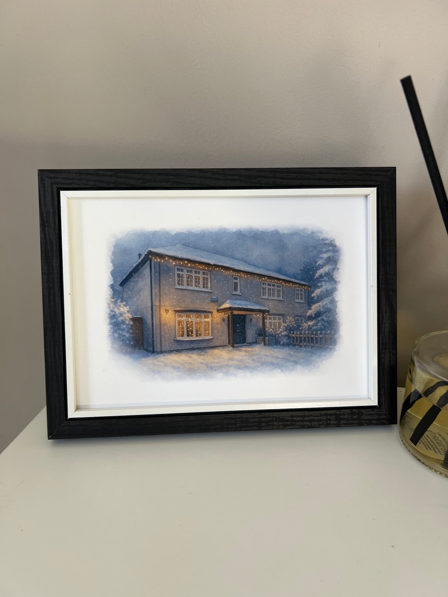 Framed artwork of a cottage style  house portrait in a winter snowy scene  in digital watercolour in a black finish frame.