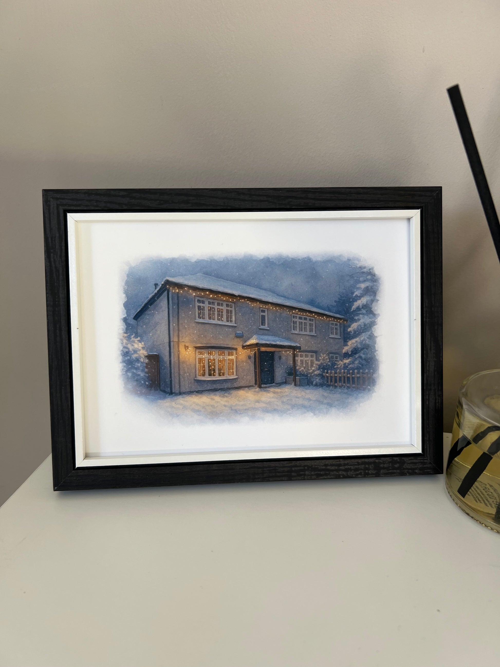 Framed artwork of a cottage style  house portrait in a winter snowy scene  in digital watercolour in a black finish frame.