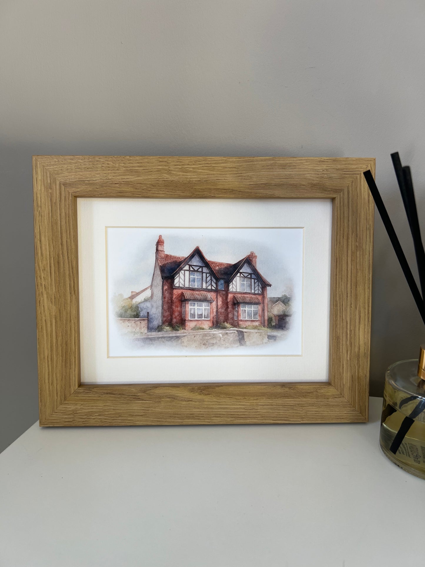 Framed artwork of a tudor style period house portrait in digital watercolour in an oak finish frame and ivory mount. 