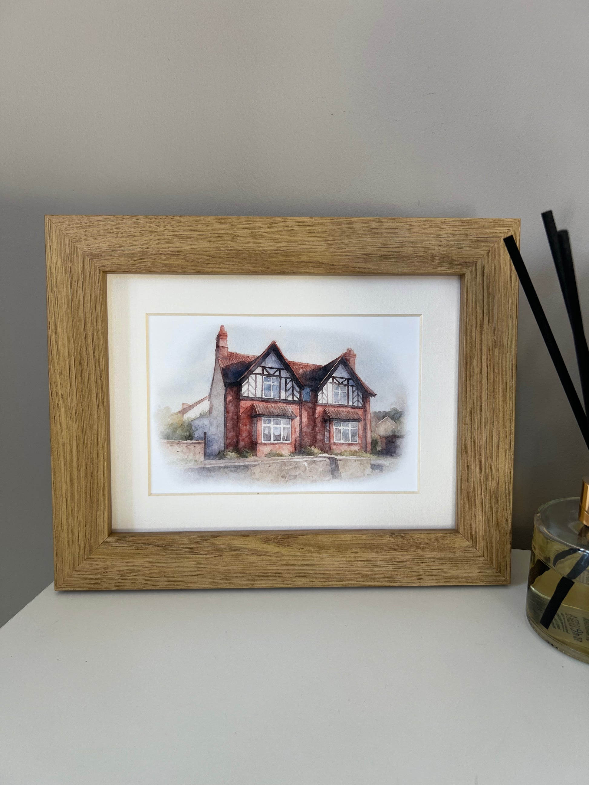 Framed artwork of a tudor style period house portrait in digital watercolour in an oak finish frame and ivory mount. 