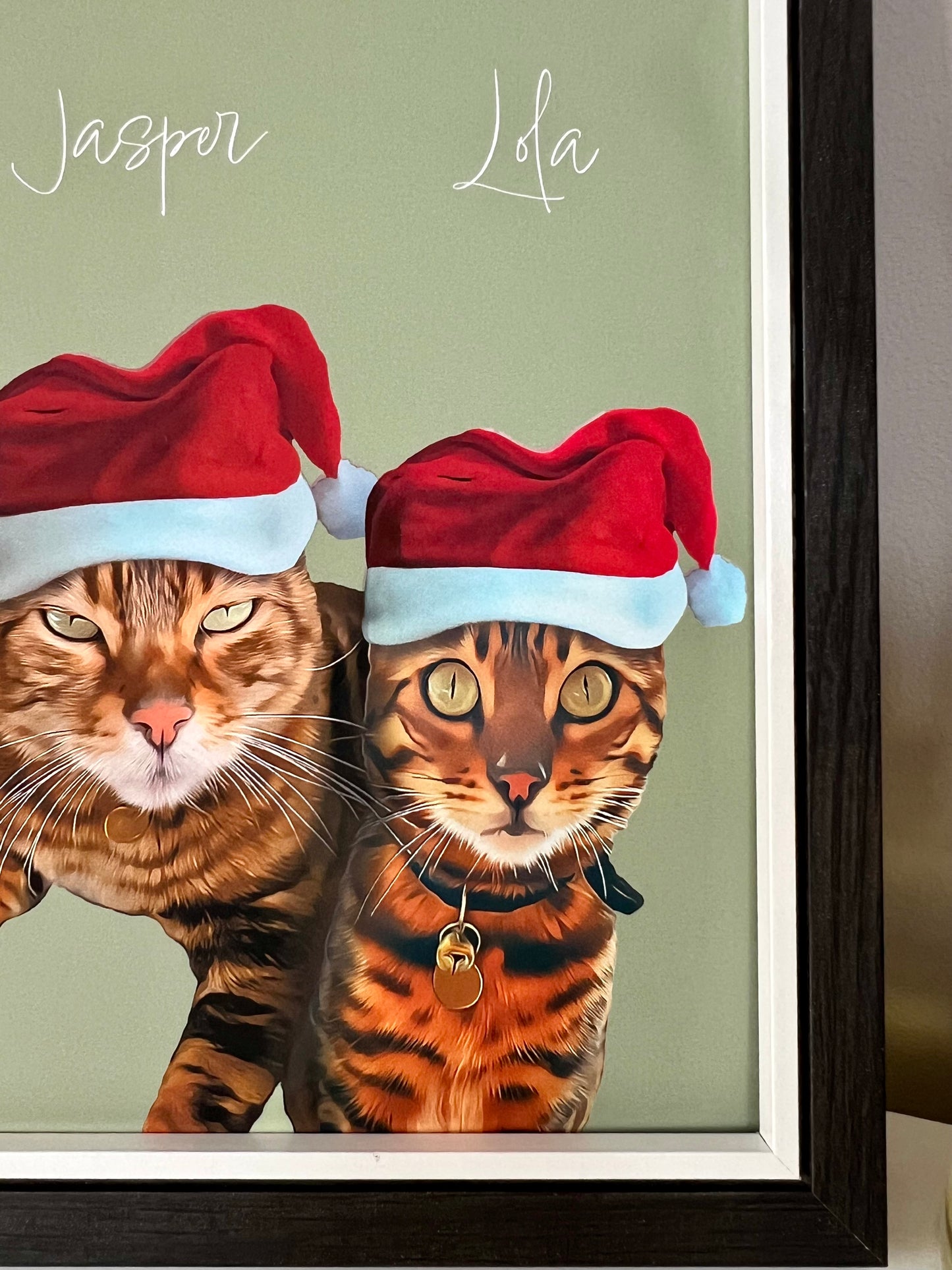 Close up right of framed artwork of two Bengal Cats wearing Santa hats in a black frame.