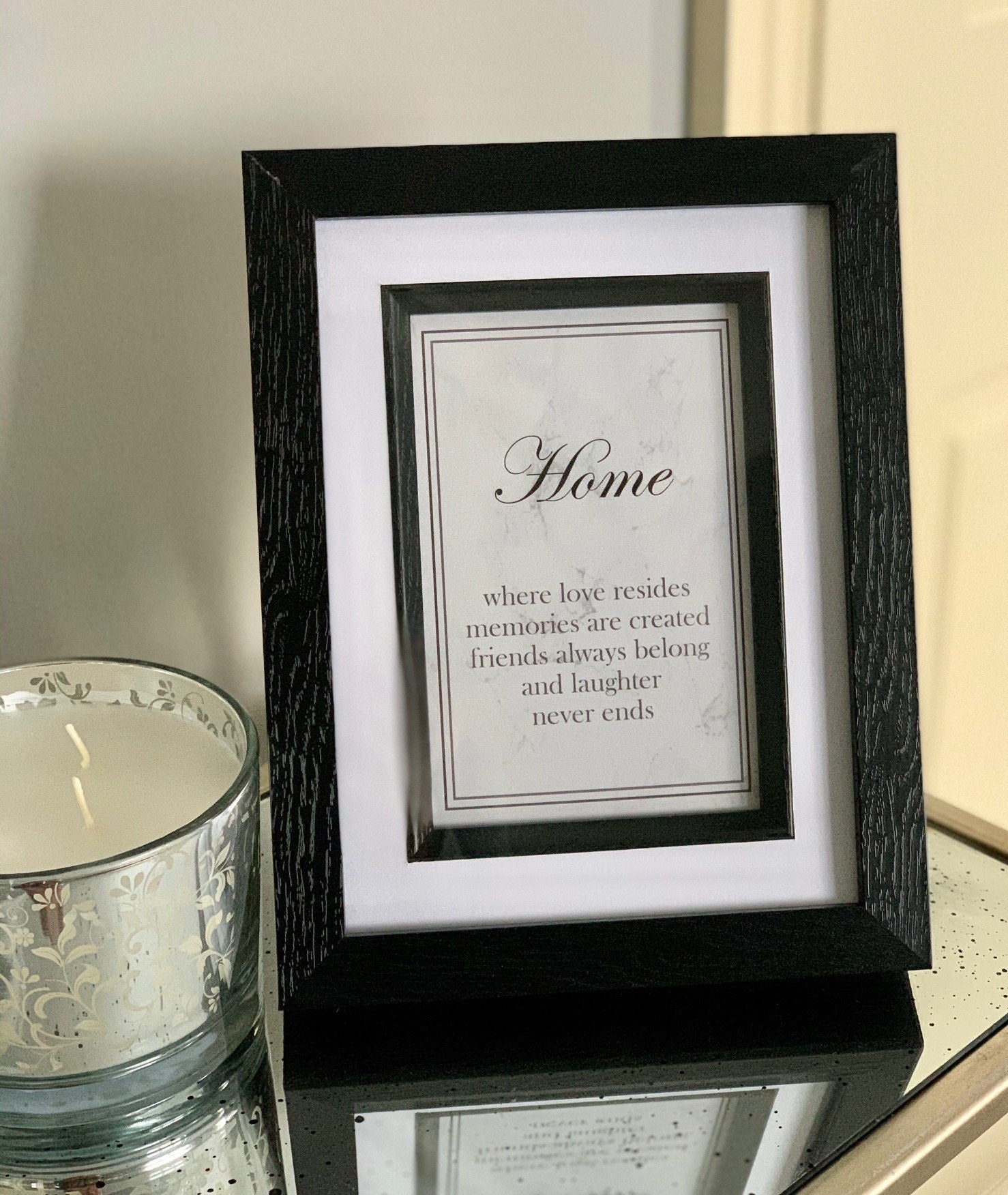 A framed print with the text 'Home - where love resides, memories are created, friends always belong, and laughter never ends' on a grey marble background and black frame.
