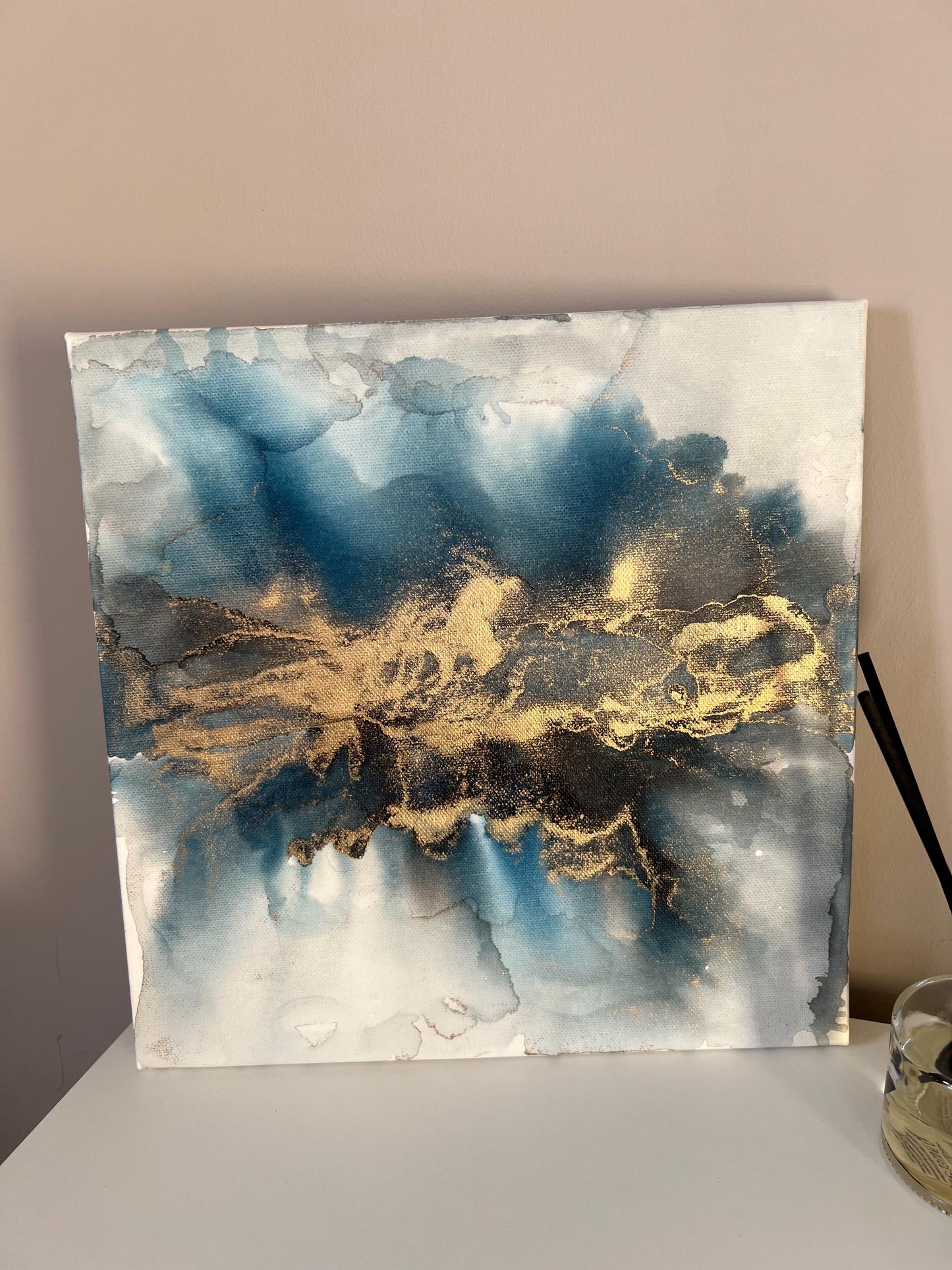 A one-off statement canvas painting featuring an abstract design in alcohol inks with gold and blue colours, with a metallic finish.