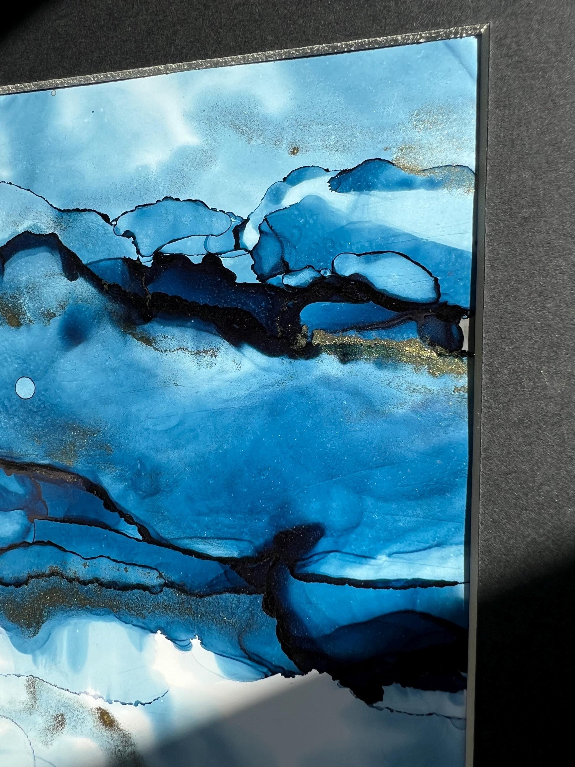 An A5 size contemporary ink painting featuring blue and metallic colors with gold shimmers, presented in a black frame.