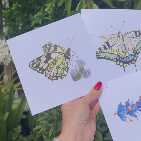 Video of Three cards with butterfly illustrations of a Marbled White, Monarch and Swallowtail all with gold and green glitter metallic accents in front of a nature background. 