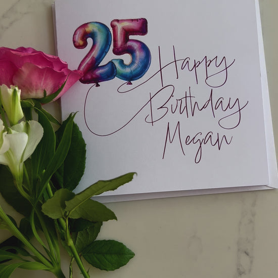 Video of a Personalised Birthday card with colourful '25' in balloons and 'Happy Birthday' text, surrounded by flowers on a marble surface.
