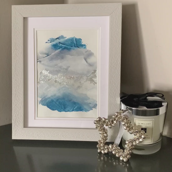 Video of a framed abstract watercolor painting with blue and grey tones, displayed on a grey shelf.