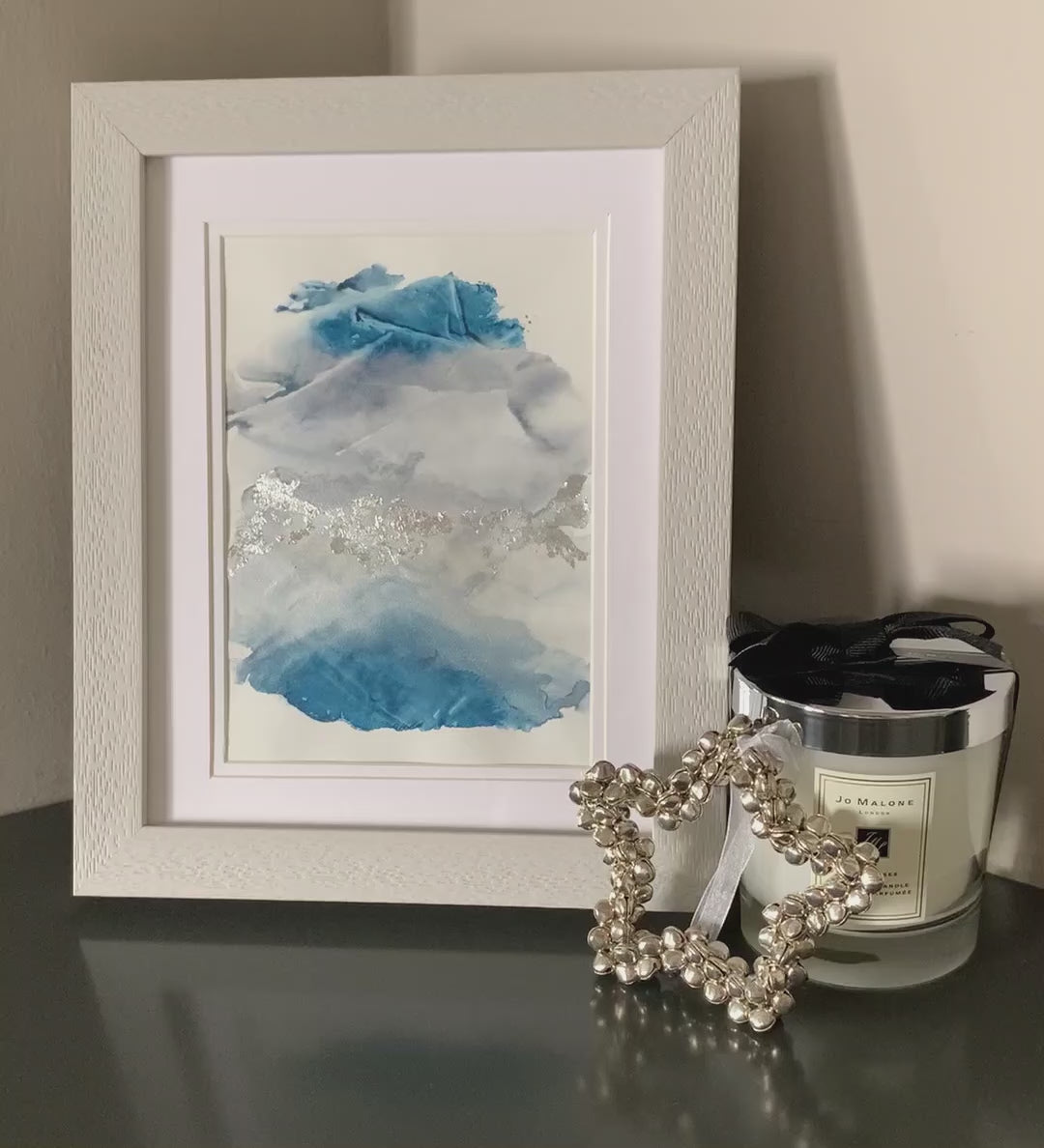 Video of a framed abstract watercolor painting with blue and grey tones, displayed on a grey shelf.
